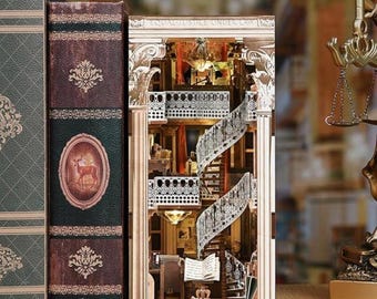 May include: A detailed wooden bookshelf diorama with a miniature interior scene. The diorama features a spiral staircase, ornate columns, and the text "EQUAL JUSTICE UNDER LAW" at the top. Adjacent to the diorama are two decorative books.