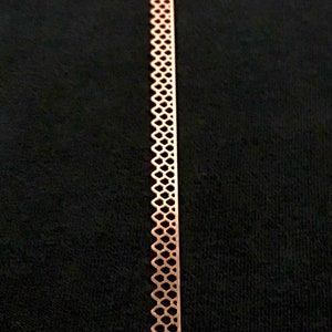 Puede incluir: Primer plano de un ribete metálico de color cobre con un patrón decorativo repetitivo de pequeños cuadrados.