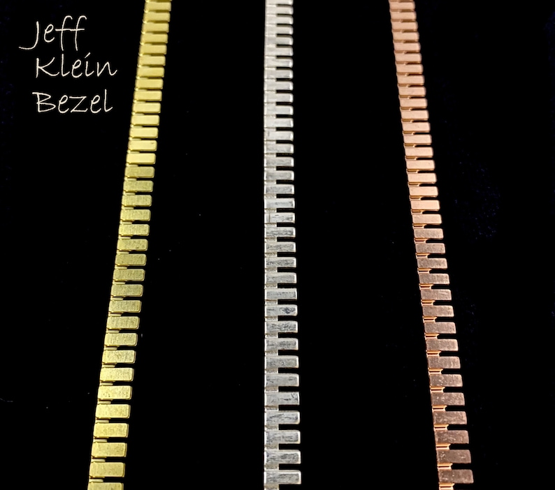 K&ouml;nnte beinhalten: Drei Metallketten, eine goldene, eine silberne und eine kupferne, werden vor einem schwarzen Hintergrund gezeigt. Die Ketten bestehen aus kleinen, rechteckigen Gliedern.