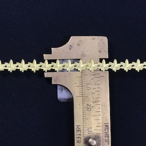 May include: A close-up of a gold-coloured leaf-shaped trim measured with a ruler. The ruler shows the trim is 1/4 inch wide.