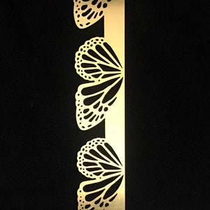 May include: A gold metal strip with a repeating pattern of butterfly cutouts. The butterflies are detailed with intricate wing designs.