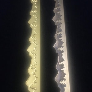 May include: Close-up of two sword blades with a wavy edge design. One blade has a gold finish, and the other has a silver finish. The blades are set against a dark background.