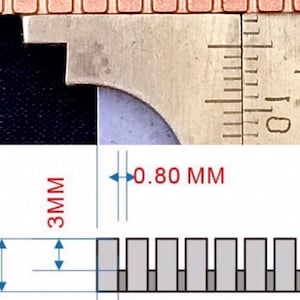 K&ouml;nnte beinhalten: Nahaufnahme eines Metalllineals mit einer Messung von 0,80 mm und 2,00 mm. Das Lineal wird verwendet, um die Breite einer Reihe kleiner, rechteckiger, kupferfarbener Objekte zu messen.