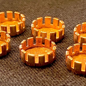May include: Six gold-coloured metal rings with a decorative, scalloped edge. The rings are arranged in a semi-circle on a brown fabric surface.