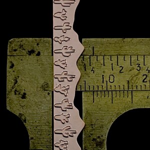May include: A close-up of a metal ruler with a decorative metal strip with a repeating pattern of cactus silhouettes. The ruler is marked in inches and the strip is about 1 1/2 inches long.