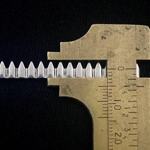 May include: Close-up of a metal gear with teeth measured by a brass caliper. The caliper shows measurements in inches.