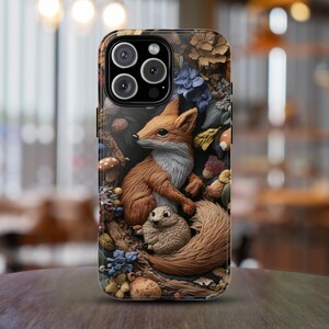 May include: A phone case featuring a detailed 3D relief design of a fox and a small rodent in a forest setting. The case has a dark background with floral and foliage elements, and the fox is rendered in shades of brown and white.