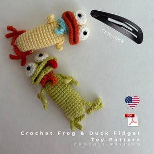 Puede incluir: Dos juguetes fidget de ganchillo: un pato amarillo con detalles en naranja y azul, y una rana verde con una lengua roja. Una horquilla negra está al lado de los juguetes. El texto dice "Click-clack" y "Crochet Frog & Duck Fidget Toy Pattern".