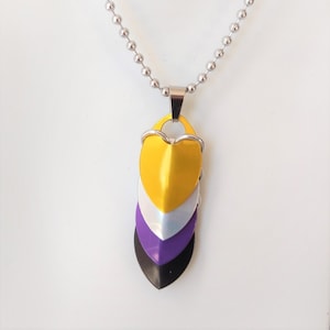 May include: A silver chain necklace with a pendant made of four layered heart-shaped pieces. The top heart is yellow, the next is white, the third is purple, and the bottom is black.