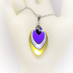 May include: A silver chain necklace with a pendant made of three layered metal leaves. The leaves are yellow, silver, and purple.