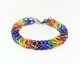 May include: A rainbow colored chainmail bracelet with a silver clasp. The bracelet is made of small metal rings that are linked together in a pattern.