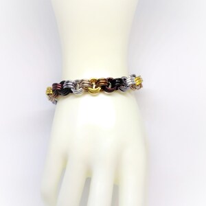Op de afbeelding: Een veelkleurige metalen armband met afwisselende schakels in goud, zilver, zwart en koper.