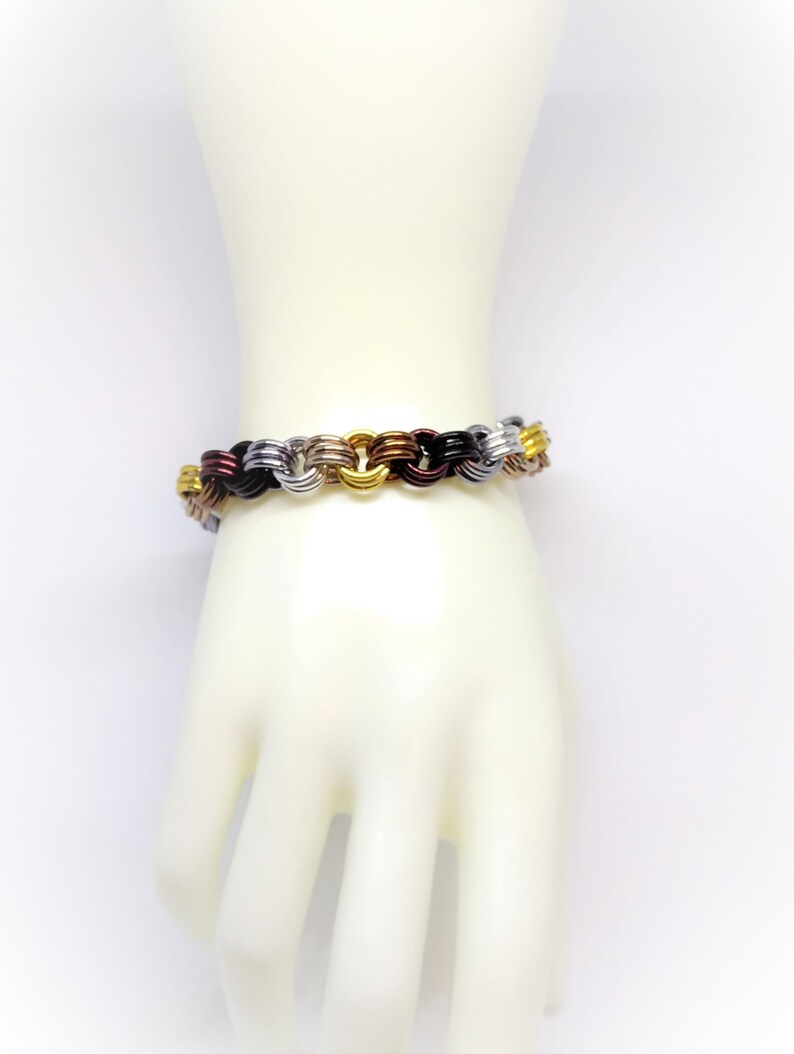 Op de afbeelding: Een veelkleurige metalen armband met afwisselende schakels in goud, zilver, zwart en koper.
