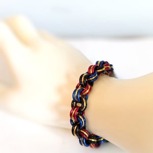 K&ouml;nnte beinhalten: Ein geflochtenes Armband aus Metallringen in den Farben Schwarz, Rot und Blau.