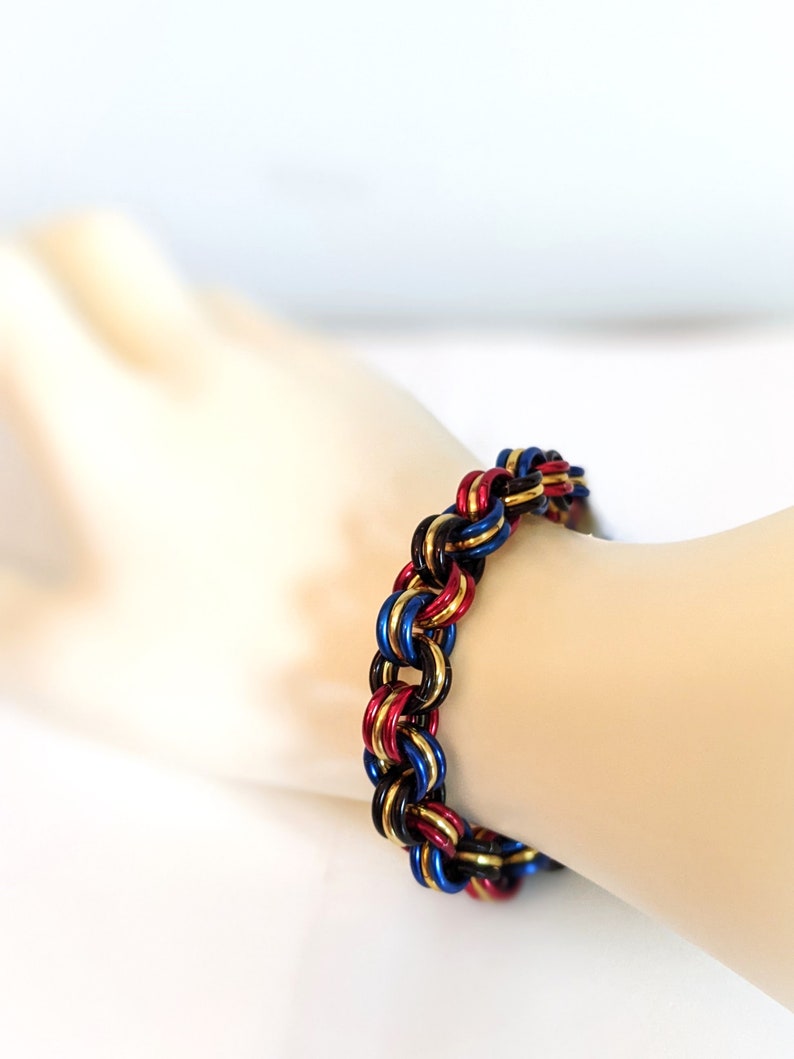 K&ouml;nnte beinhalten: Ein geflochtenes Armband aus Metallringen in den Farben Schwarz, Rot und Blau.
