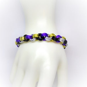 May include: A purple, black, and gold chain bracelet. The bracelet is made of metal and has a woven design.