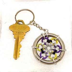 May include: A silver key chain with a purple, yellow, and black wire-wrapped charm in the shape of a flower. The key chain also has a gold key with the number 70665 on it.