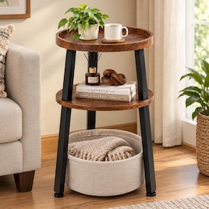 May include: A three-tier round side table with a dark wood grain finish and black metal legs. The top shelf holds a potted plant and a white mug. The middle shelf displays a reed diffuser, wooden chain links, and two books titled The Kinfolk Home and Simple Matters.