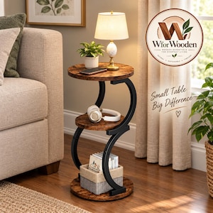 May include: A three-tier round side table with a rustic brown wood-grain finish and a black metal S-shaped frame. The table features three circular shelves, a small white basket on the bottom shelf, and a pair of white headphones on the middle shelf.