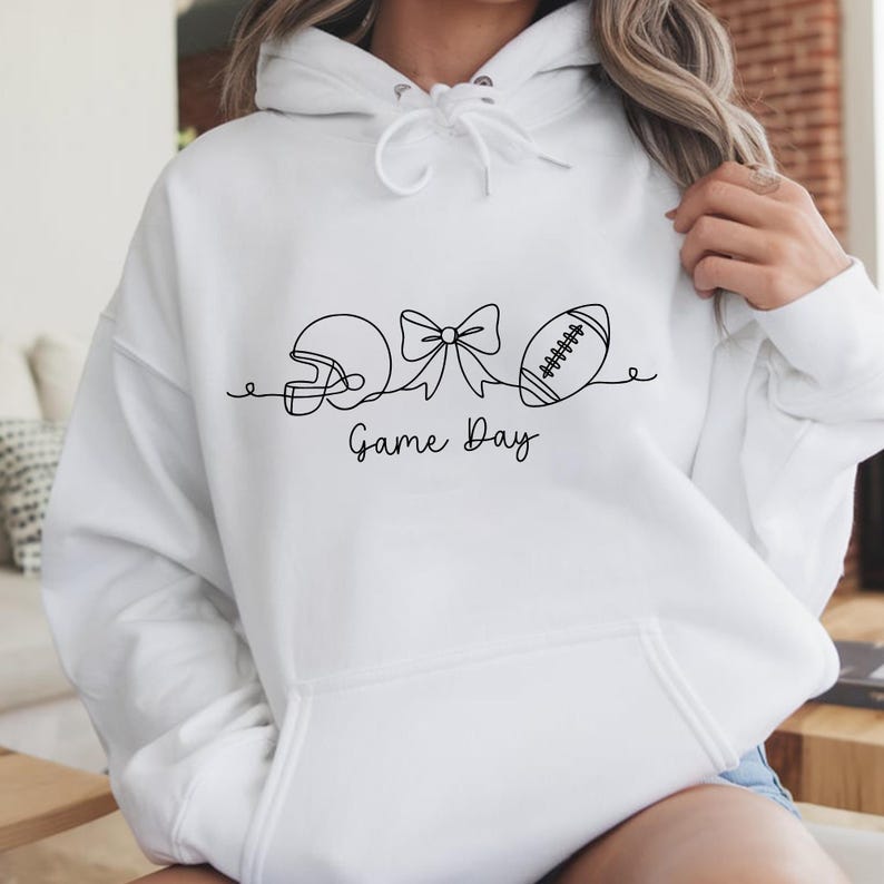 Pode incluir: Moletom branco com um desenho de linha preta de um capacete de futebol americano, um la&ccedil;o e uma bola de futebol. As palavras "Game Day" est&atilde;o escritas abaixo. O moletom tem capuz com cord&atilde;o e um bolso frontal.