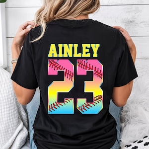Pu&ograve; includere: Maglietta nera con il nome "AINLEY" e il numero "23" in colori arcobaleno con un design a pallina da softball.