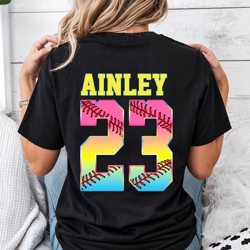 Pu&ograve; includere: Maglietta nera con il nome "AINLEY" e il numero "23" in colori arcobaleno con un design a pallina da softball.