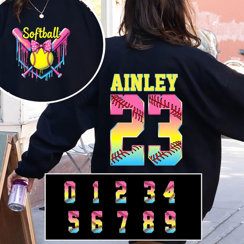 Pu&ograve; includere: Felpa nera con un design a forma di palla da softball e il nome "AINLEY" e il numero "23" sul retro. I numeri sono arcobaleno con un design a punto di softball. La parte anteriore della felpa ha una palla da softball con un fiocco rosa e vernice che cola. I numeri da 0 a 9 sono mostrati in colori arcobaleno con un design a punto di softball.