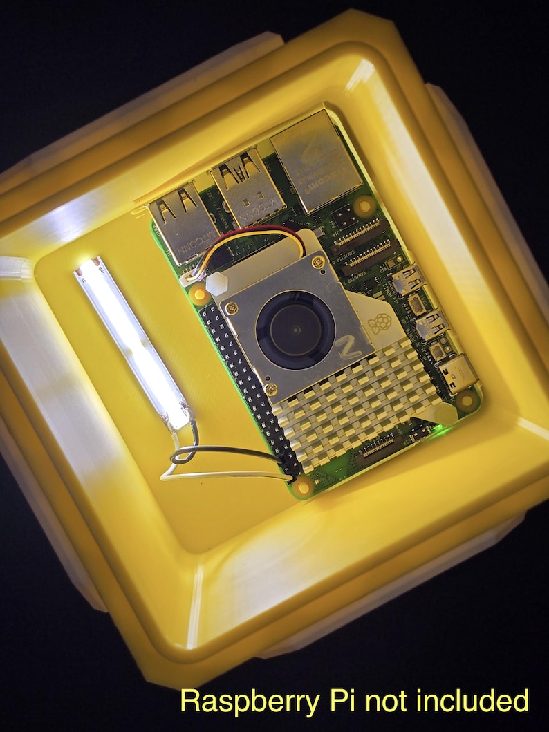May include: A yellow plastic case with a green circuit board inside. The circuit board has a small fan and a heat sink. The text "Raspberry Pi not included" is printed below the case.
