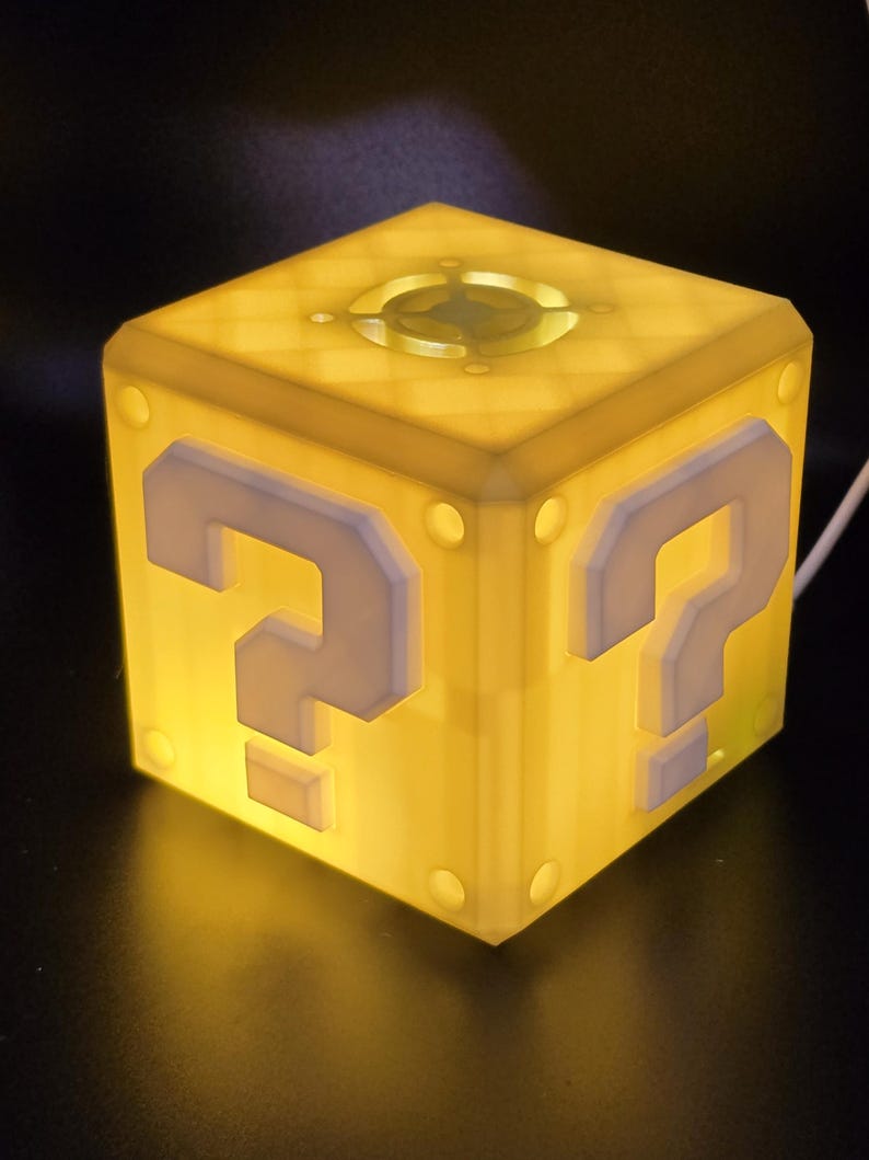 May include: A yellow cube-shaped night light with a question mark on each side. The light is on and glowing.