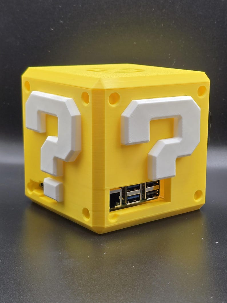 May include: A yellow 3D printed box with a question mark on each side. The box has a slot for a USB cable and a slot for a power cable.