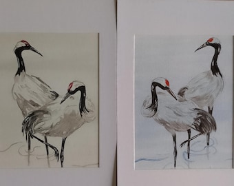 Puede incluir: Dos pinturas de acuarela de grullas japonesas. Las aves tienen plumas blancas y grises, cuellos negros y coronas rojas. Están de pie en aguas poco profundas, con un lavado azul claro que sugiere la superficie del agua. Las pinturas están enmarcadas en blanco.