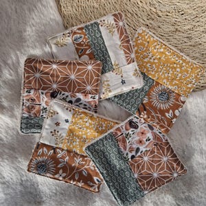 Op de afbeelding: Een verzameling van zes vierkante stoffen onderzetters. Elke onderzetter heeft een patchwork-ontwerp met verschillende patronen, waaronder geometrische vormen, bloemenprints en botanische motieven. Het kleurenpalet omvat tinten bruin, geel, wit en groen.