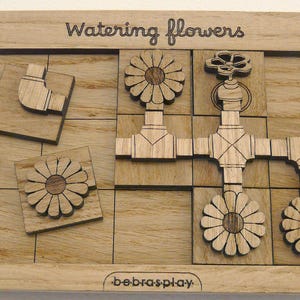 Könnte beinhalten: Holzpuzzle-Spiel mit dem Titel "Watering flowers" und dem Markennamen "bebrasplay". Das Puzzle enthält verschiedene Holzstücke, darunter Blumen, Rohre und einen Wasserhahn.