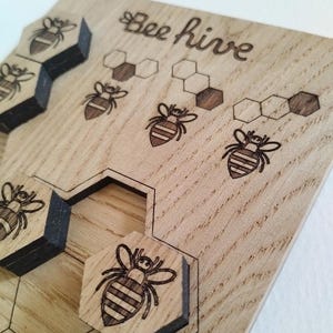 Op de afbeelding: Houten puzzel met een bijenkorf thema. De puzzel heeft een houten bord met een honingraatpatroon en verschillende bijen. De tekst "Bee Hive" staat op het bord.