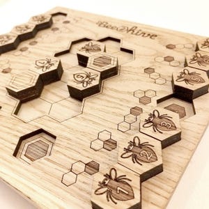 Op de afbeelding: Een houten spelbord met een honingraatpatroon en bij-vormige stukken. Het bord is gelabeld "Bee Hive".