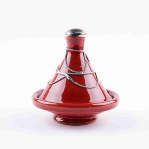 Peut inclure: Un tajine en céramique rouge avec une poignée et une chaîne décorative en métal argenté. Le tajine a un couvercle conique et une base large et peu profonde. Le pot est conçu pour la cuisine et le service de plats marocains.