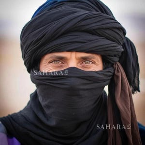 May include: A person wearing a black turban and face covering. The person's eyes are visible, and the text "SAHARA 45" is printed on the lower right and left of the image. The turban is a dark color, and the background is blurred.