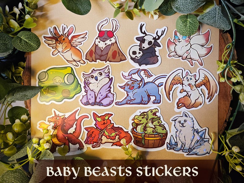 May include: A selection of Baby Beasts stickers showcasing a variety of fantastical creatures. Designs include a winged rabbit, a moth, a creature with a skull, a nine-tailed fox, a frog, an owl, a blue cat-like beast, a winged cat, a dragon, and more.