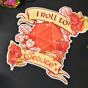 May include: A sticker with a red D20 die surrounded by red and pink roses. The banner above reads "I roll to", and the banner below reads "Seduce". The sticker has a holographic effect.