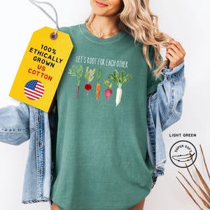 A light green t-shirt with the text 'Let's root for each other' and a row of five watercolor illustrations of different vegetables.