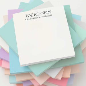 May include: A stack of pastel-colored square notepads. The top notepad is white with the text "ZOE KENNEDY OCCUPATIONAL THERAPIST" in black. The other notepads are various shades of pink, blue, green, and lavender.