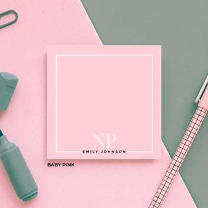 May include: A baby pink notepad with a white border, the initials "NP" and the name "Emily Johnson" are printed on the notepad. The notepad is on a pink and green background with a pen and marker.