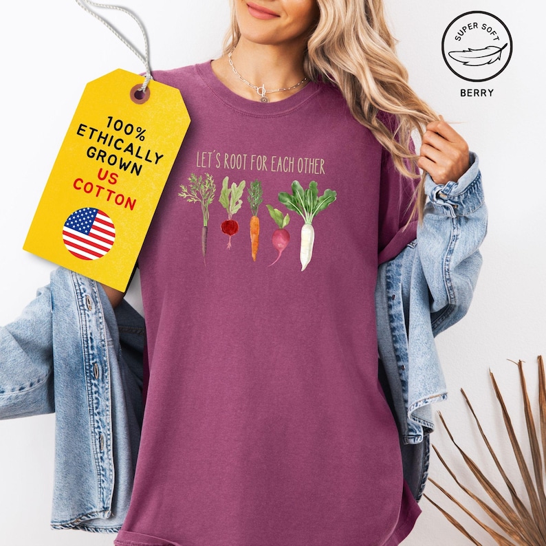 A berry colored t-shirt with the text 'Let's root for each other' and a graphic of five vegetables: a carrot, a radish, a turnip, a beet, and a white radish.