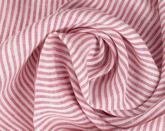May include: Pink and white striped fabric with a textured linen weave. The fabric is folded and draped, showing the pattern and texture.