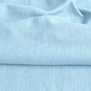 Könnte beinhalten: Nahaufnahme eines hellblauen Stoffes mit strukturierter Oberfläche. Der Stoff ist in der Mitte gefaltet und erzeugt einen weichen, fließenden Effekt.