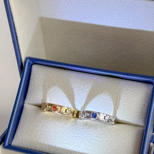 Può includere: Due anelli in oro e argento con pietre preziose rosse e blu in una scatola per anelli in velluto blu.