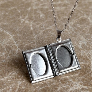 May include: Silver chain necklace with a silver locket pendant that opens to reveal two oval-shaped photo slots.