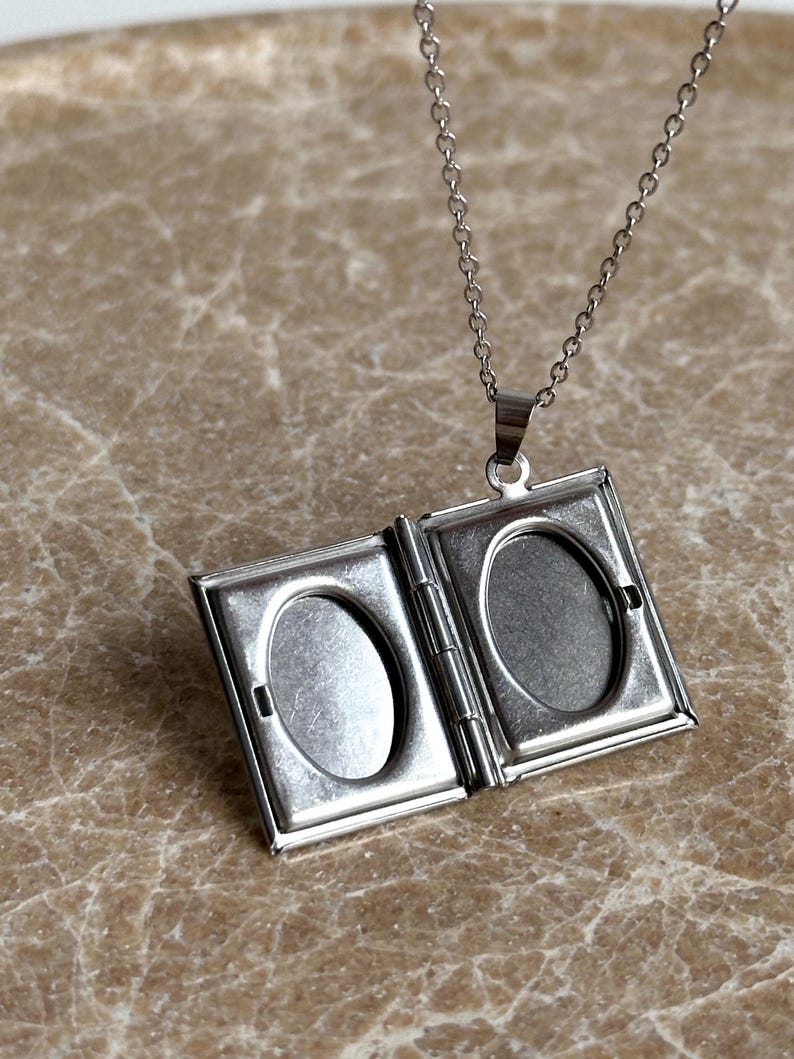 May include: Silver chain necklace with a silver locket pendant that opens to reveal two oval-shaped photo slots.