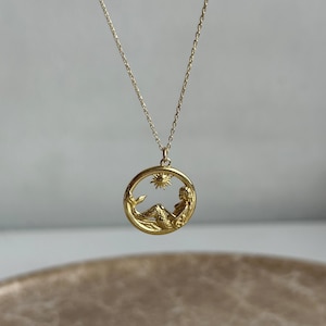 May include: Gold necklace with a circular pendant featuring a mermaid sitting under a sun. The pendant is detailed and has a textured finish.