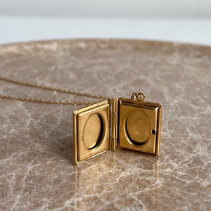 May include: A gold-toned locket necklace with a book-shaped pendant. The locket opens to reveal two oval-shaped compartments.